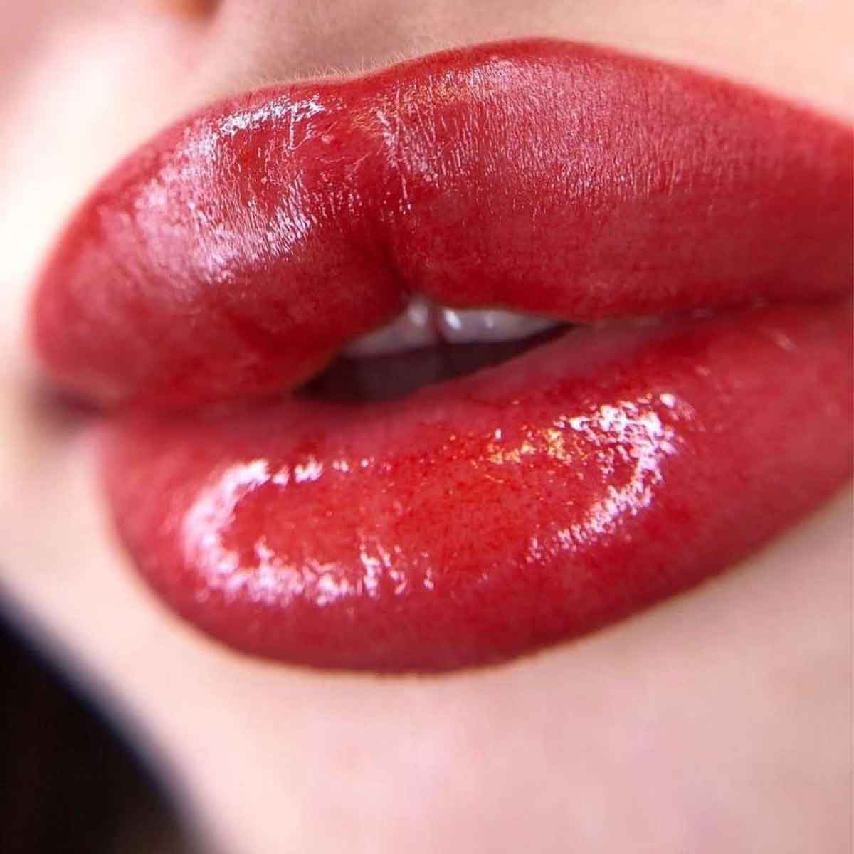 Close-up of glossy red lips wearing a vibrant red lip gloss or lipstick.