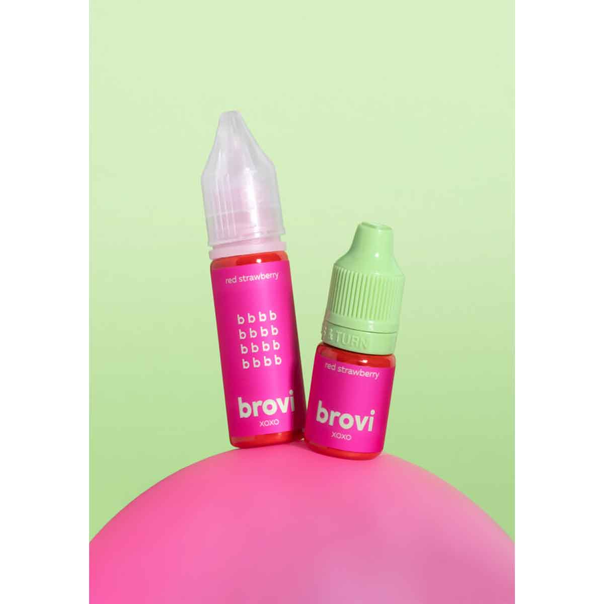 Two Brovi e-liquid bottles, one larger pink bottle and one smaller green-capped bottle, both labeled 'hot strawberry' and 'brovi', displayed on a pink surface against a light green background.