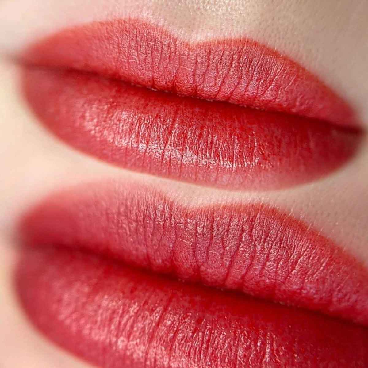 Close-up of lips wearing a glossy, deep red lipstick with visible lip texture and a soft sheen.