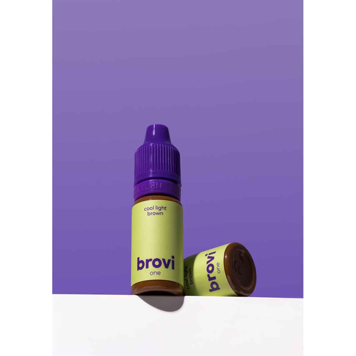 Two Brovi One e-liquid bottles in the 'cool light brown' flavor, featuring a light green label and purple caps, set against a solid purple background with one bottle lying on its side.