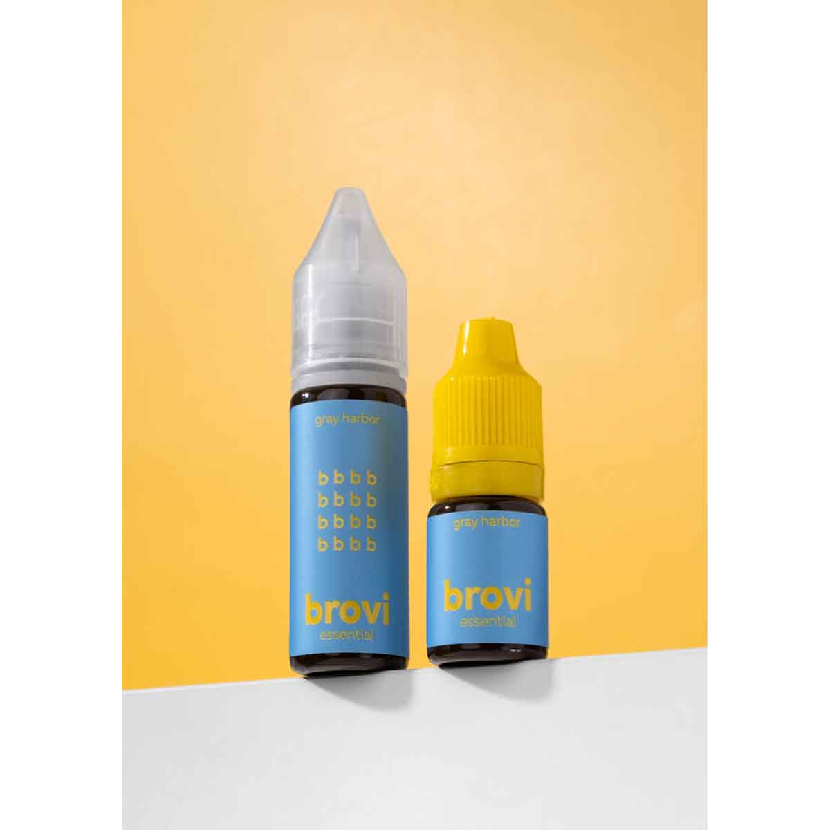 Two Brovi e-liquid bottles standing upright on a white surface against a yellow background. One bottle has a clear cap and a blue label with yellow text, and the other has a yellow cap and a matching blue label.